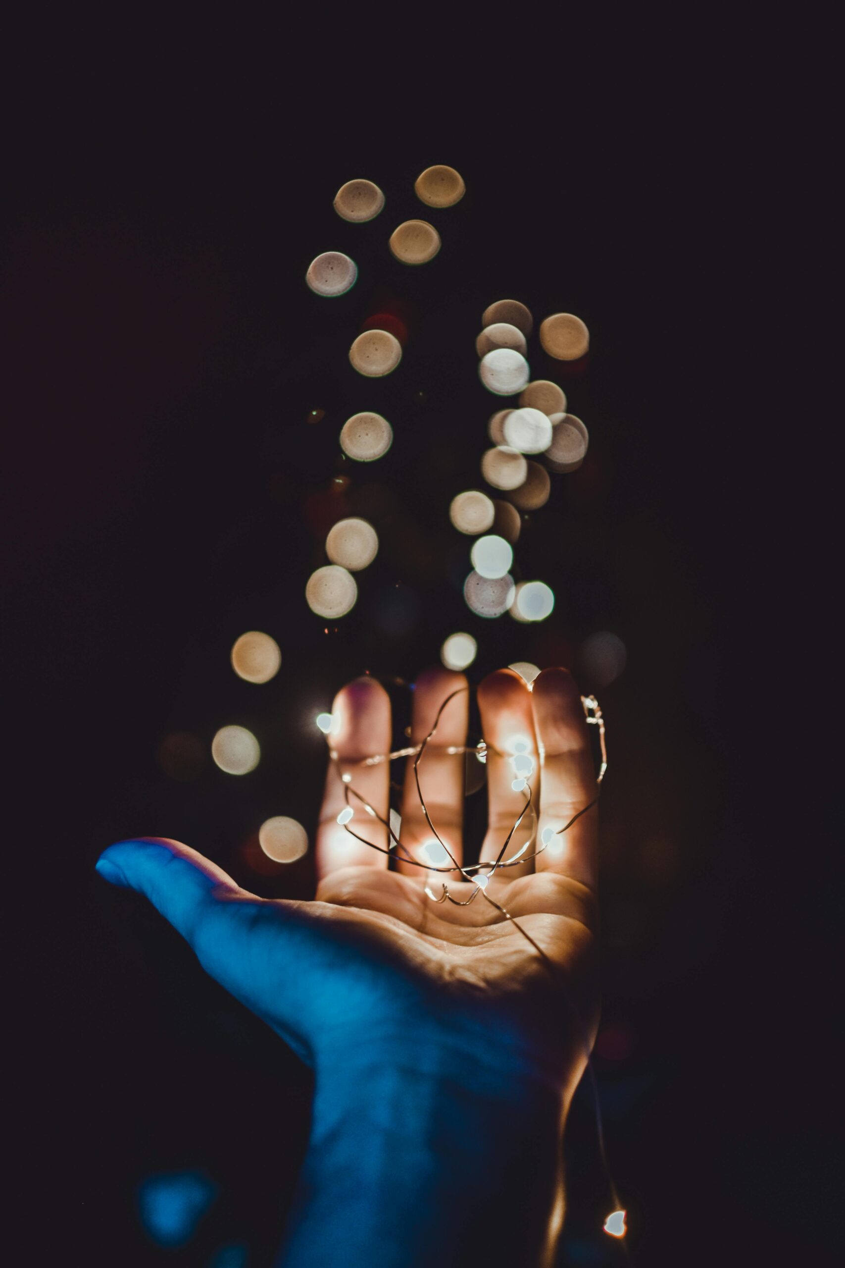 A close-up of a hand holding glowing string lights with a beautiful bokeh effect in the background.